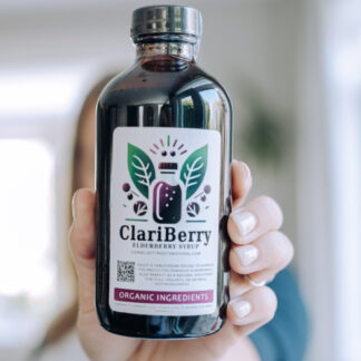 Woman holding Elderberry Syrup bottle far in front of her.
