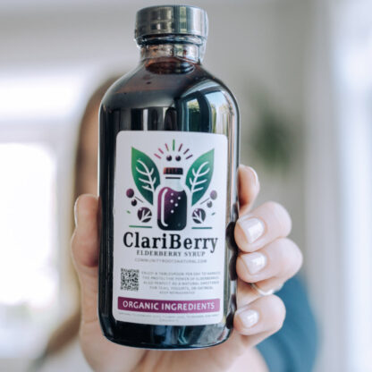 Woman holding Elderberry Syrup bottle far in front of her.