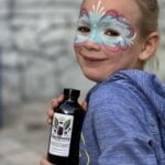 Small girl with faceprinting poses with a bottle of Clariberry Elderberry Syrup.